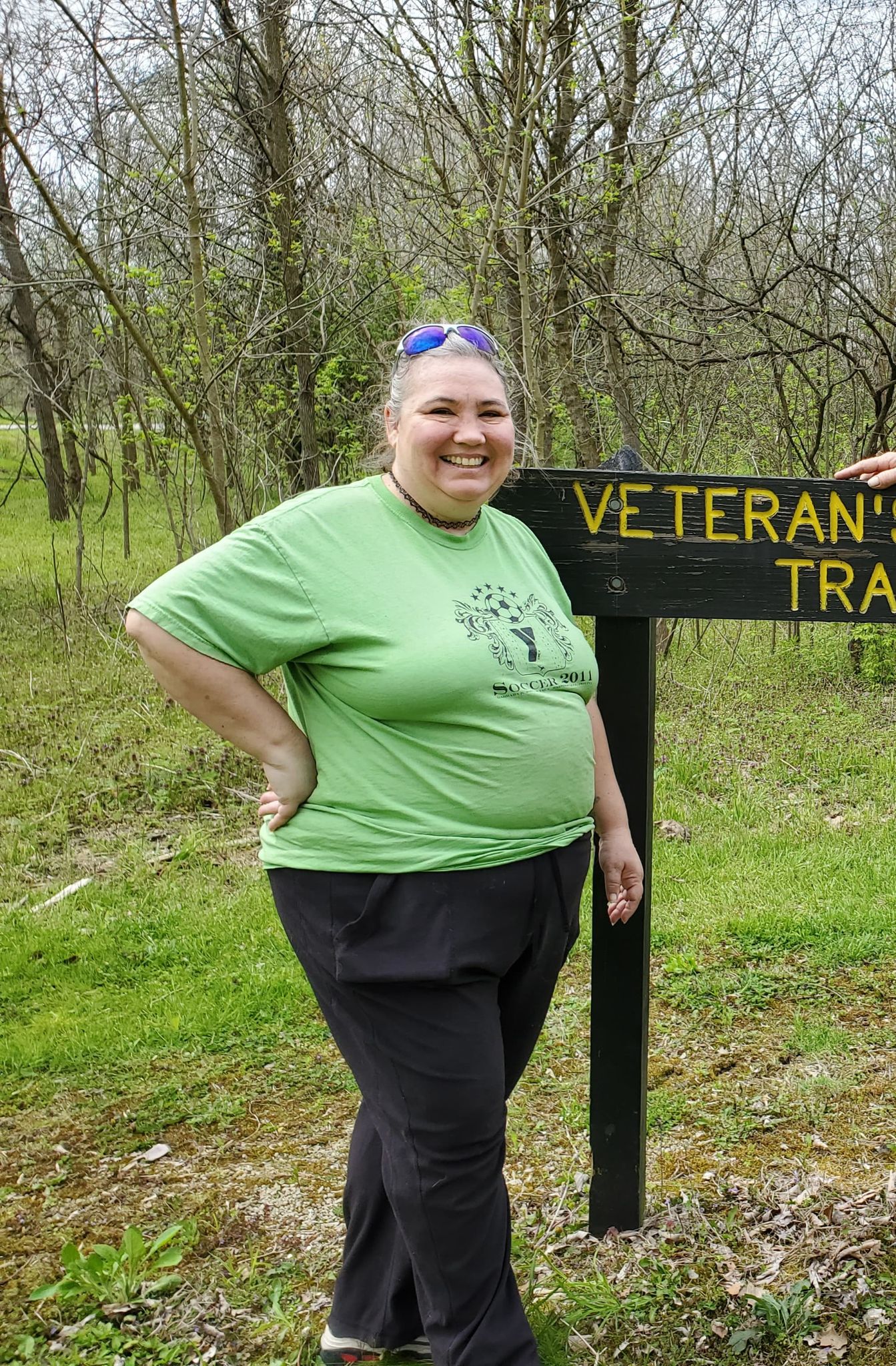 cathy-demoss wearing a green shirt and brown pants in the woods