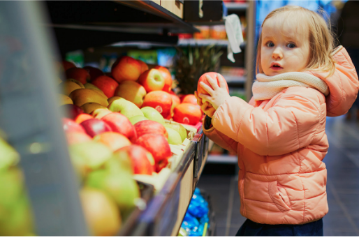 a child holding an apple on the supermarket produce section