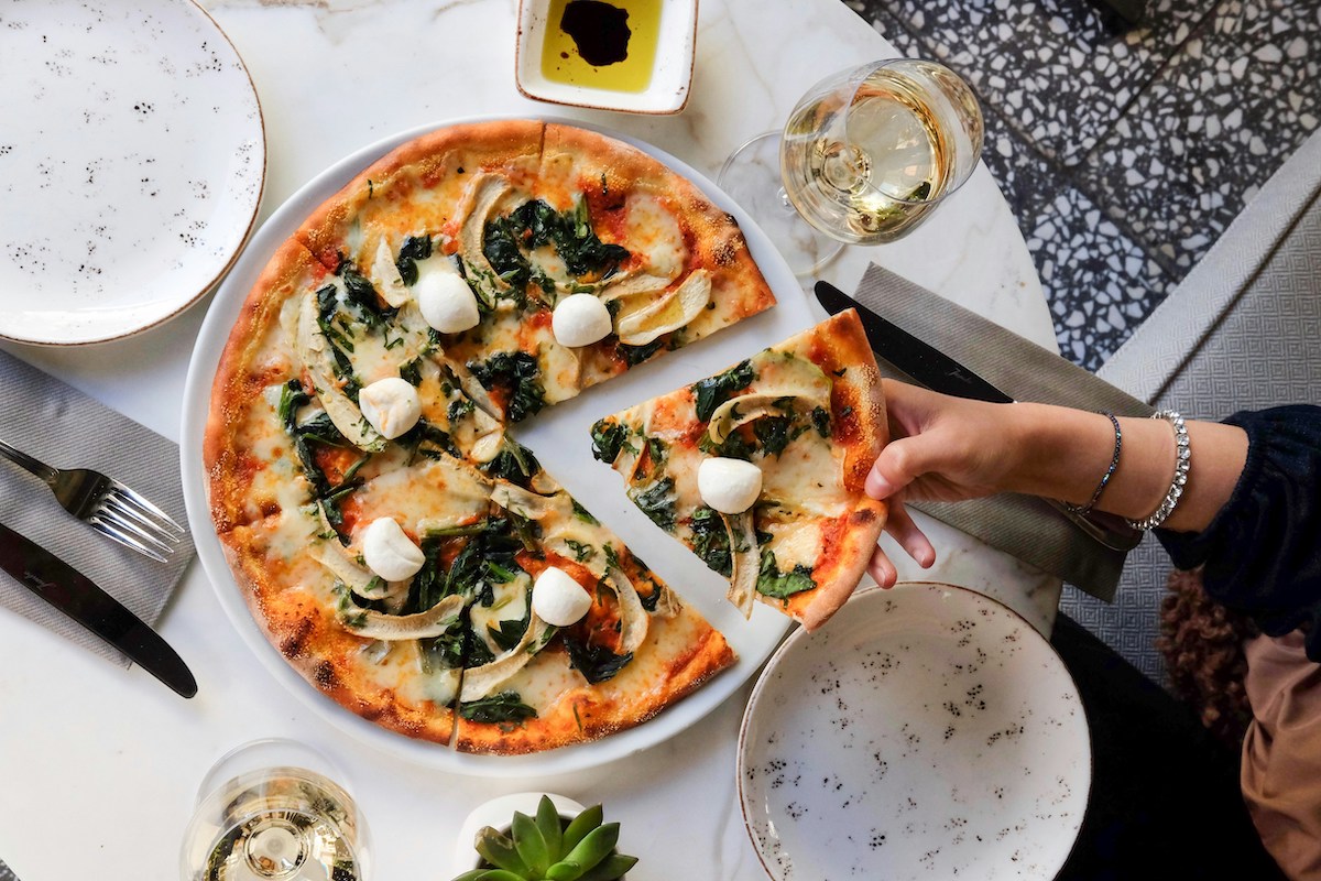 someon taking a piece of pizza from a pizza on a plate 