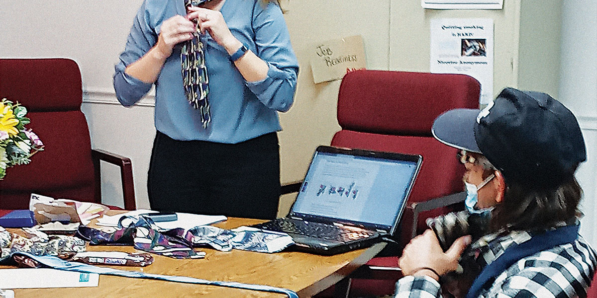 Mary Foell, LaPorte County Community Development Extension Educator, helps a participant in the Work Ready course practice tying a tie.