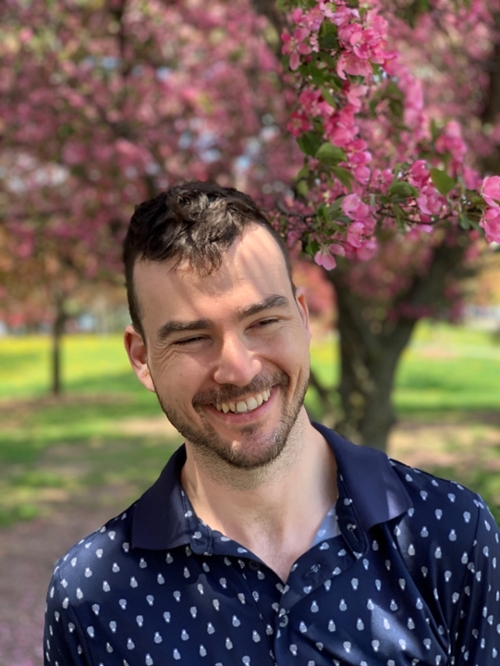 Dr. David Wallace-Hare smiling in front of Purdue flowering trees