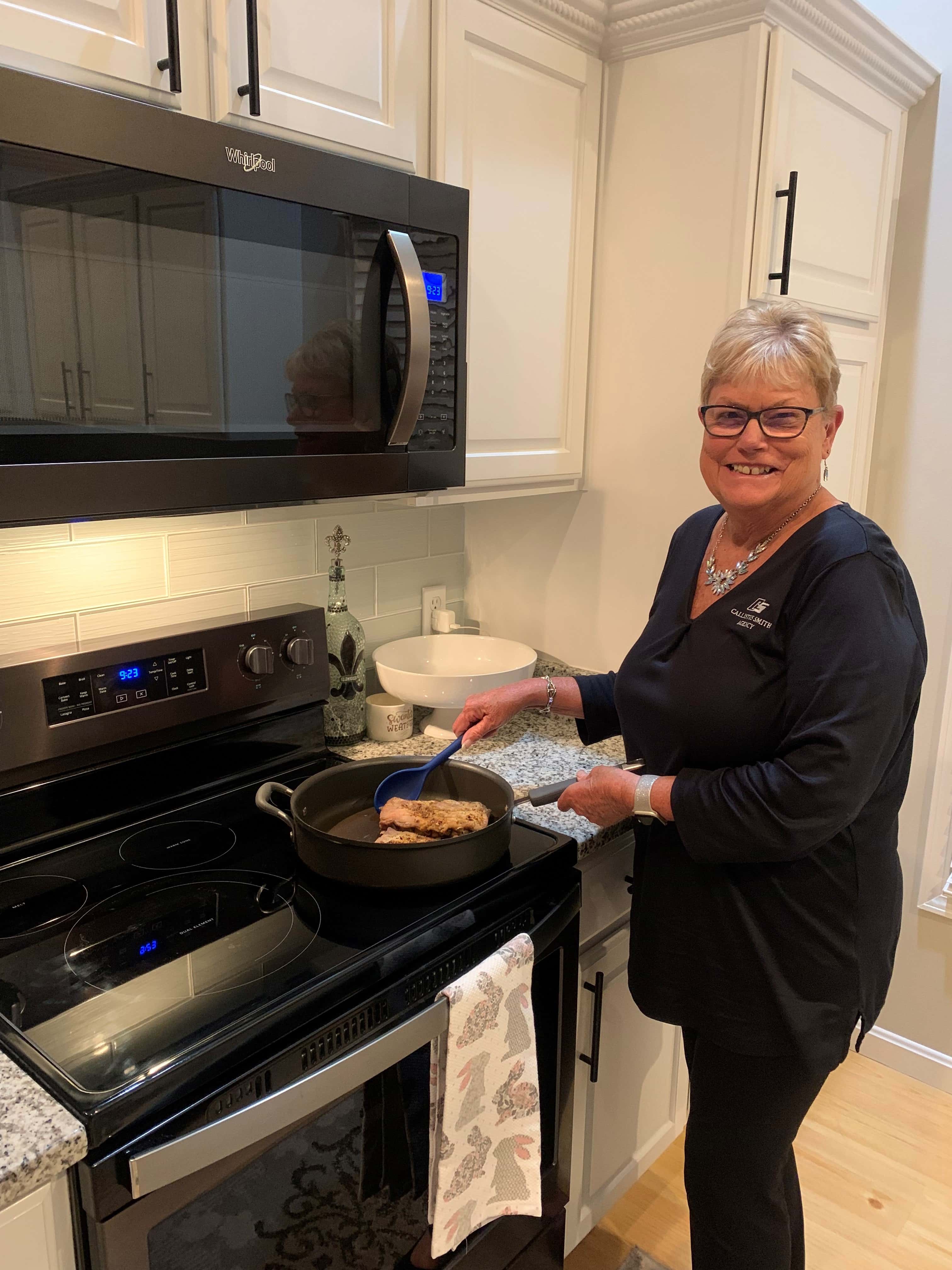 Peggy Fawcett stands in kitchen next to oven holding a cooked dish.