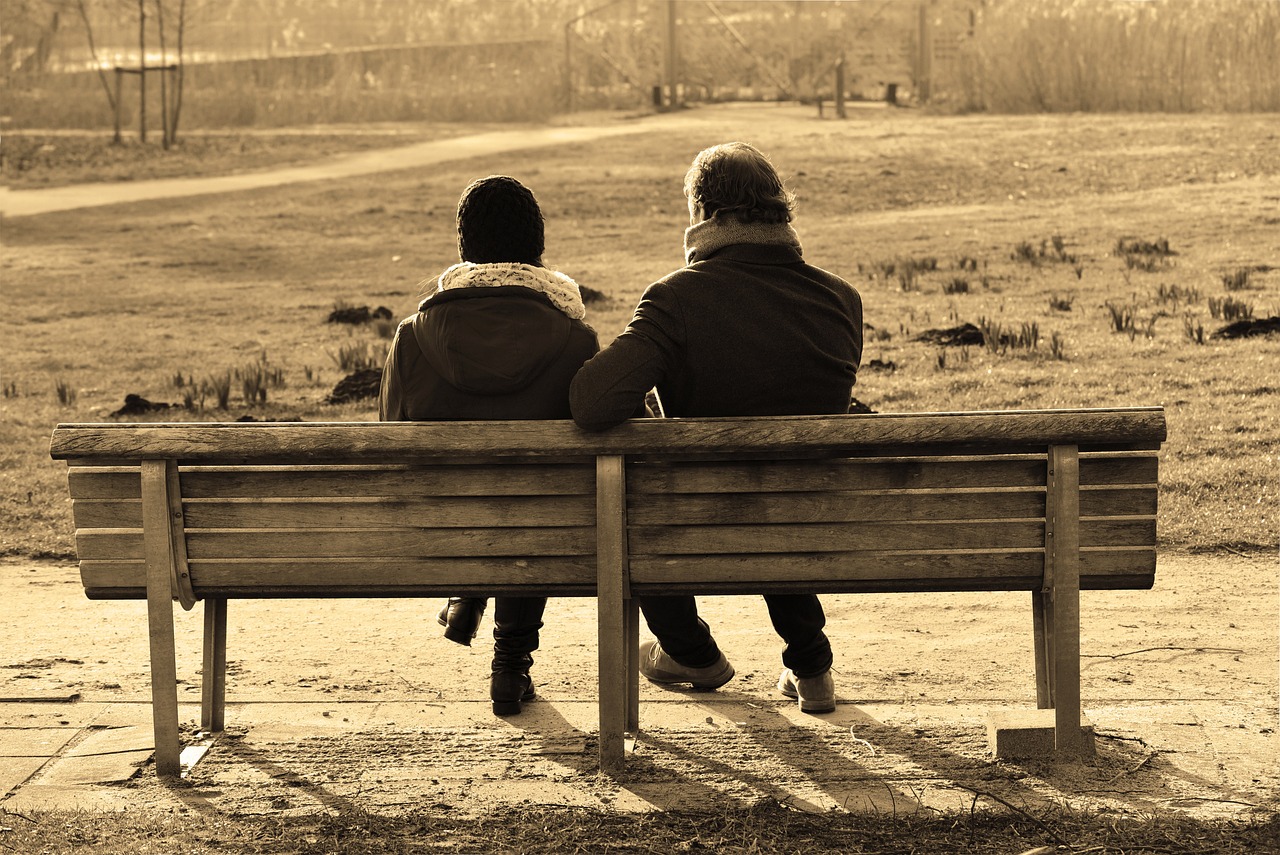 a young man and a grown man sit on a bench and talk