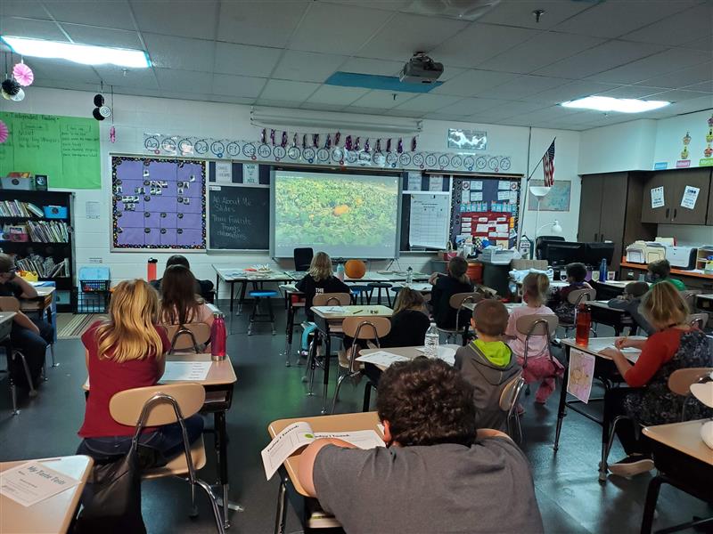 Students in desks watch a video about pumpkins.