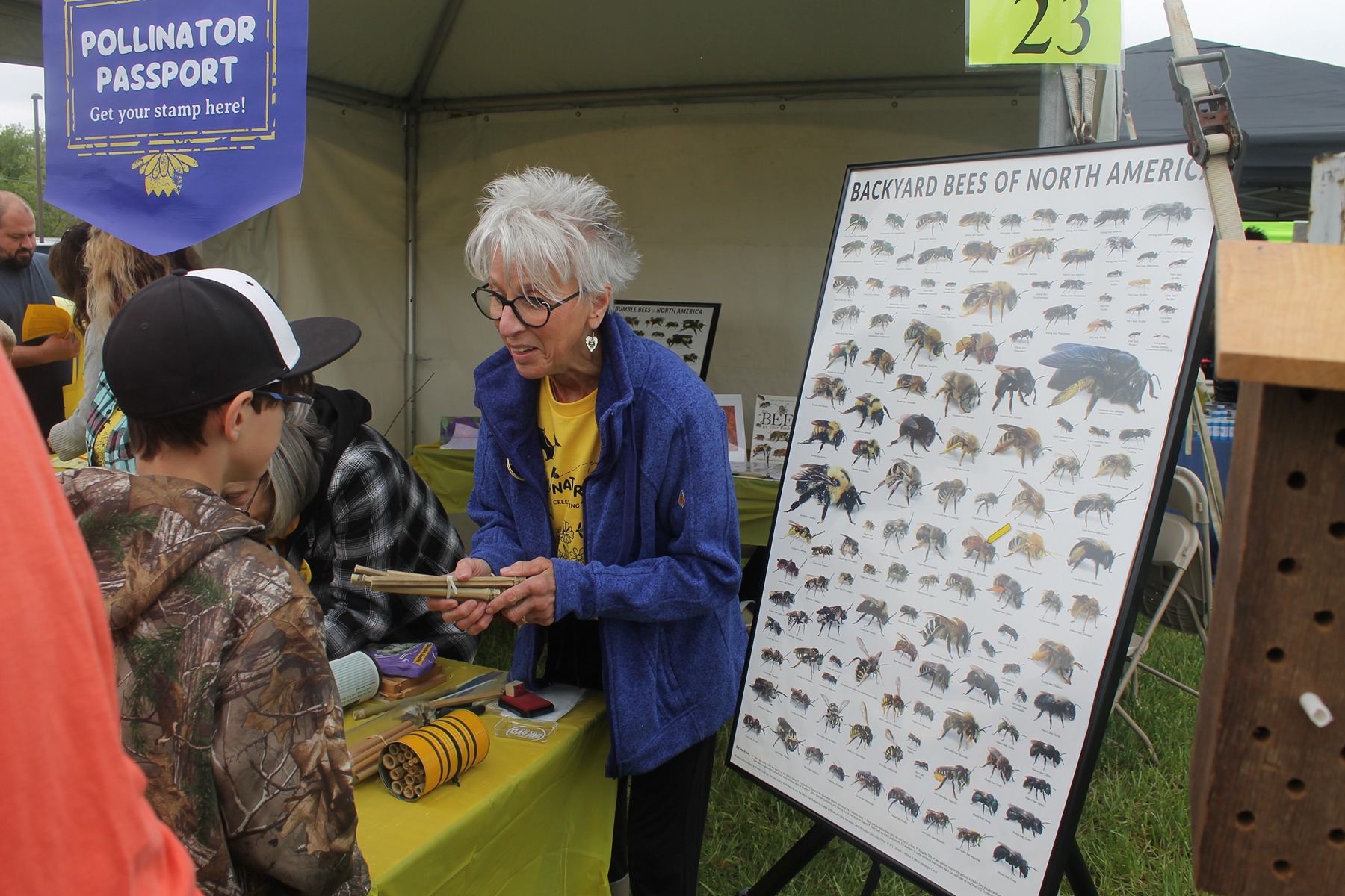 A volunteer stands at a booth next to  a poster of backyard bees