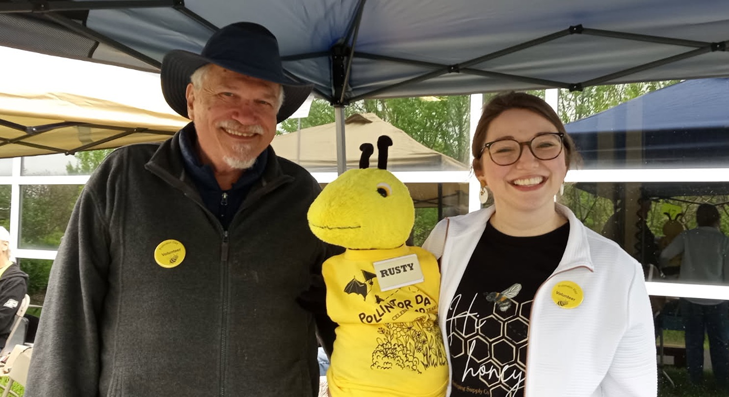 Two volunteers pose with stuffed mascot Rusty the Bee