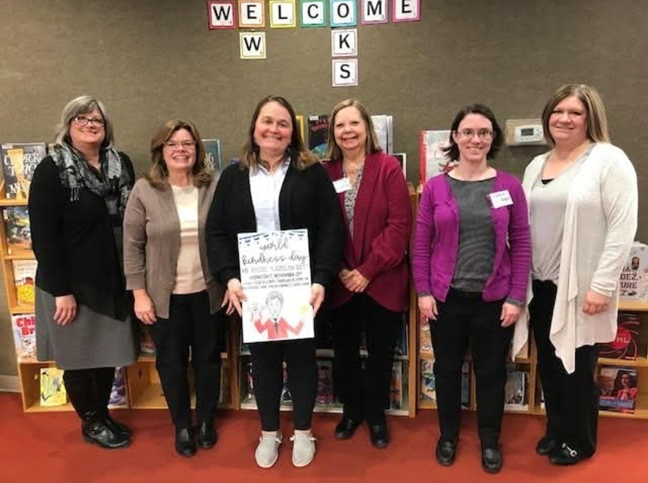 Shelly Powell holds a sign for "World Kindness Day" next to her co-workers at the library.