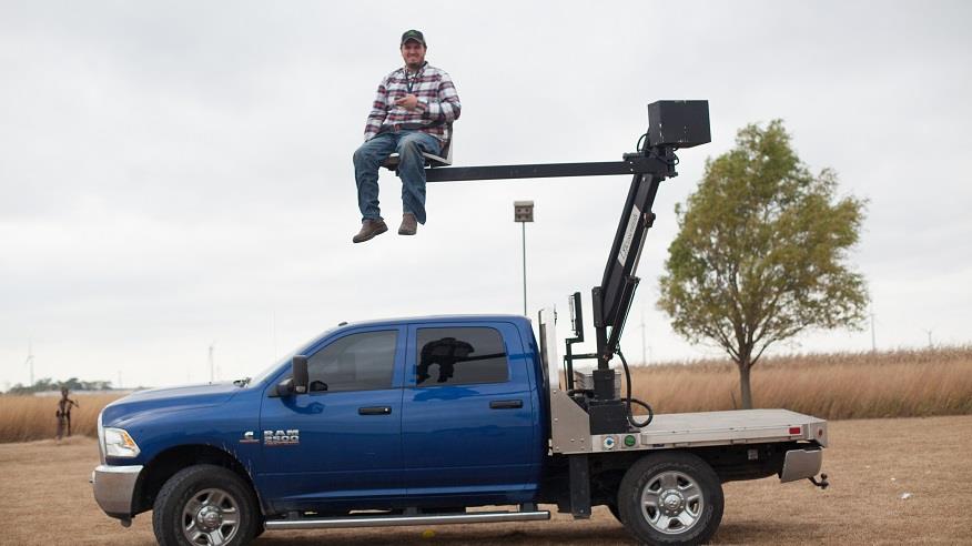 A man sits in a chair lift attached to a pickup truck