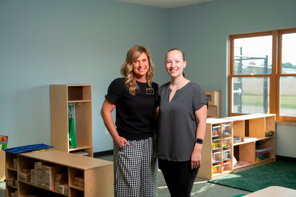A woman is standing in a childcare center and smiling.
