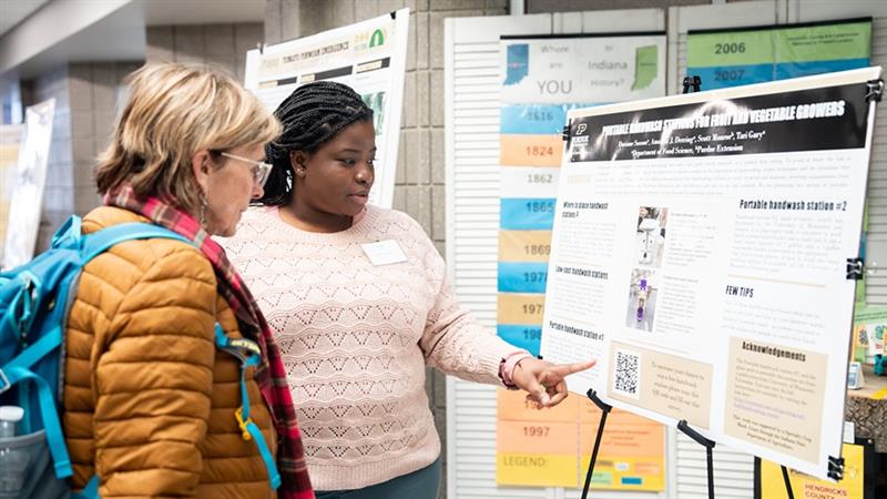A Purdue student shows her research poster to a conference attendee
