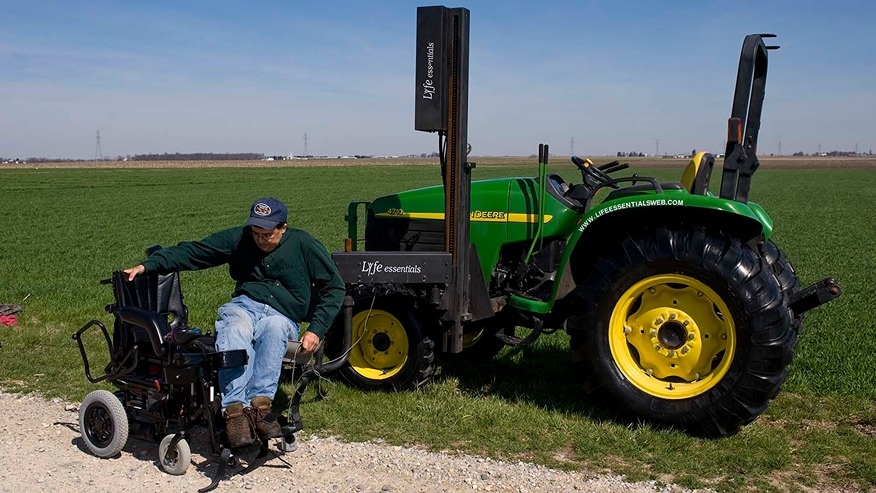 A man transfers from an assistive seat lift on a tractor into a wheelchair