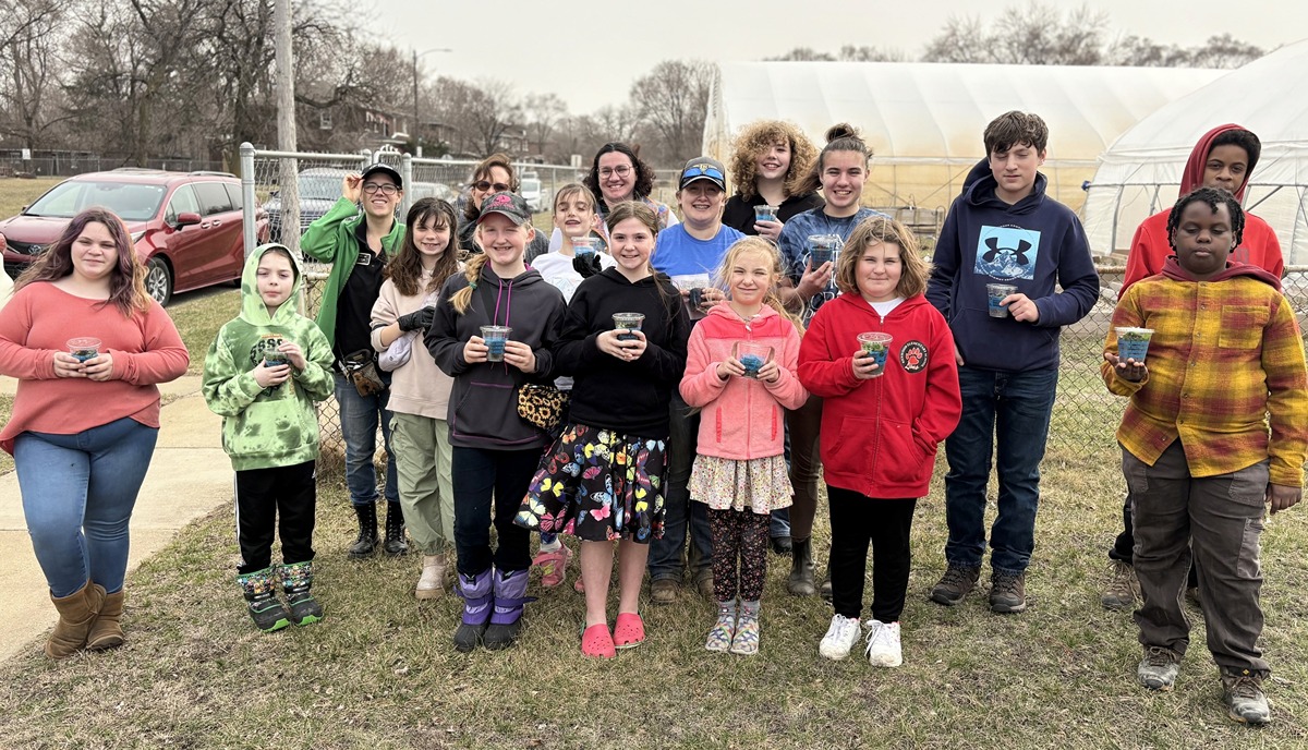 A group of 14 youth hold cups with soil next to three adult leaders.
