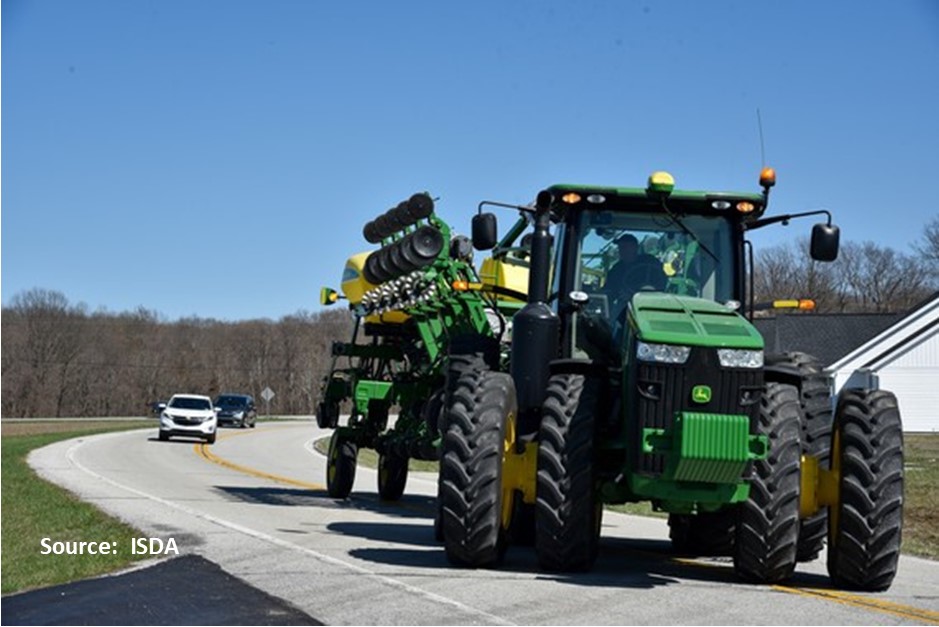 Image of a tracktor in a public road, two cars behind