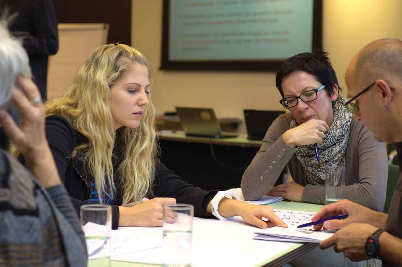 A group of diverse adults conversing around a table during a meeting.